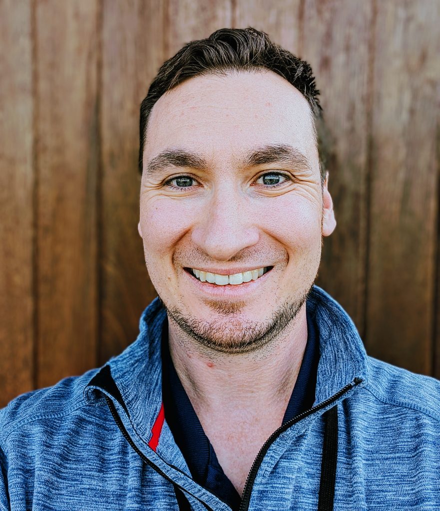 Picture of a man wearing a blue sweater and smiling at the camera.